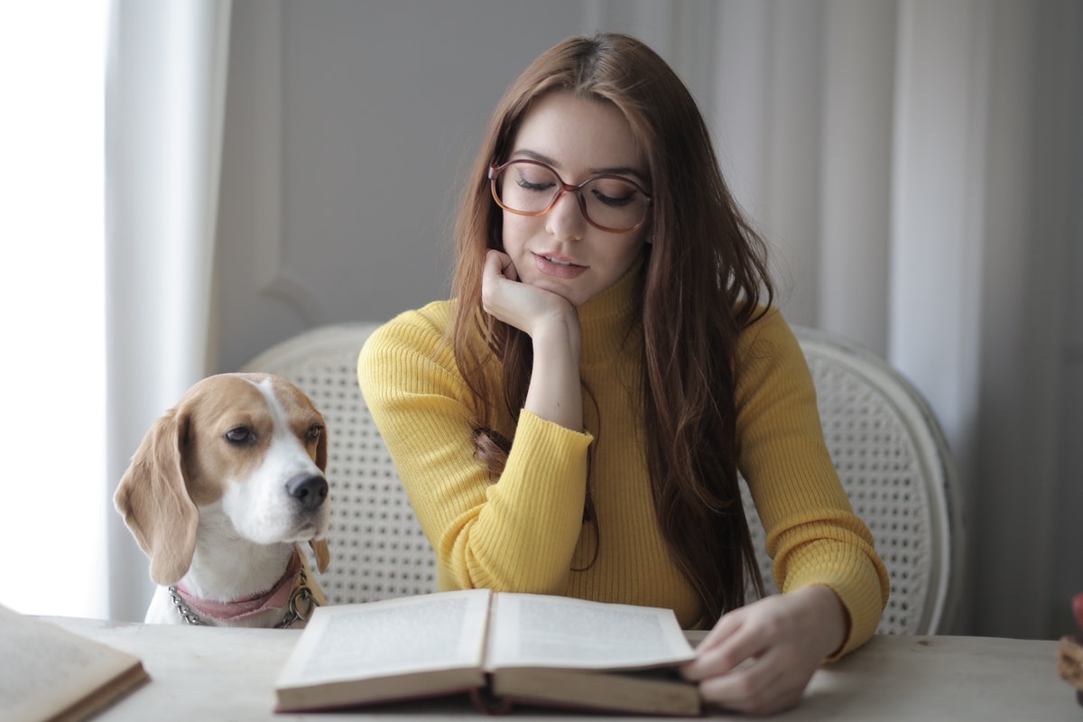 Szemüveges nő könyvet olvas a kutyájval. A moringa kalciumtartalma a tejét is felülmúlja